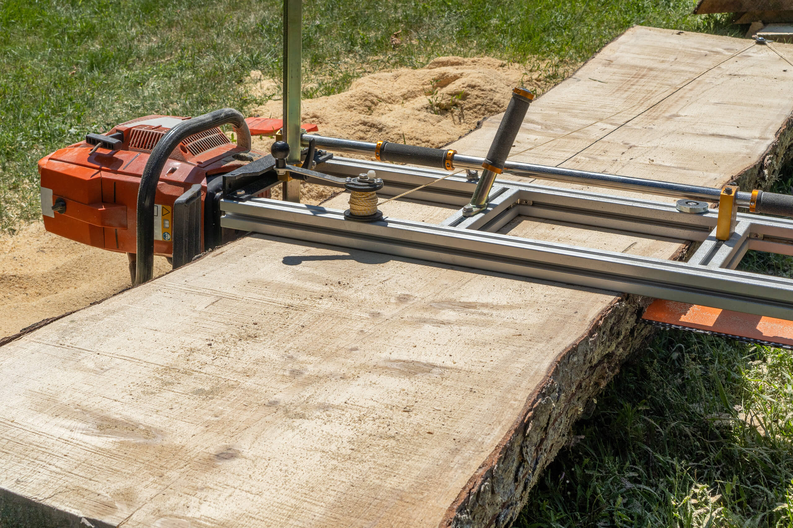 Portable chainsaw mill cutting a wide slab from a large log in a yard.